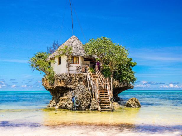 Ein kleines Haus mit Strohdach steht auf einem Felsen im türkisfarbenen Wasser.