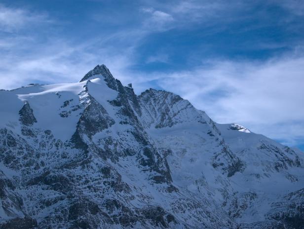 Der schneebedeckte Großglockner unter einem blauen Himmel mit Wolken.