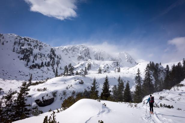Eine Person geht mit Skiern in einer verschneiten Berglandschaft.