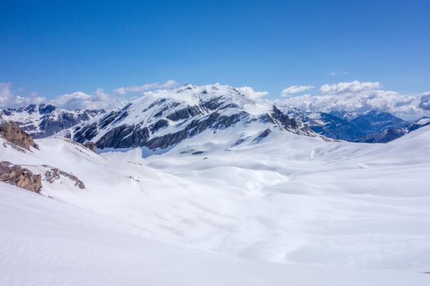 Eine weite, schneebedeckte Berglandschaft unter blauem Himmel.