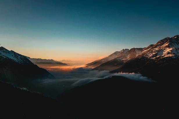 Eine Berglandschaft mit schneebedeckten Gipfeln und Nebel in den Tälern bei Sonnenaufgang.