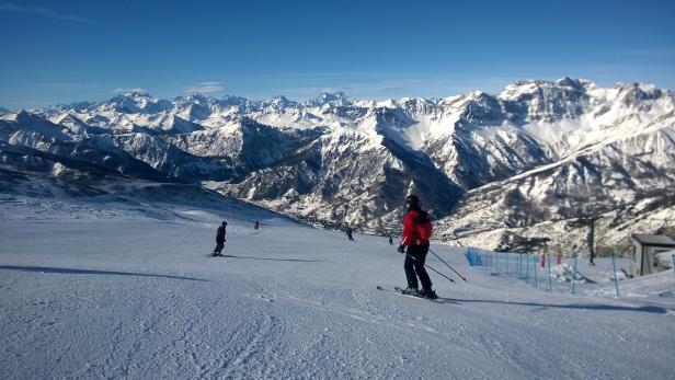 Eine Skifahrerin auf einer Skipiste mit schneebedeckten Bergen im Hintergrund.