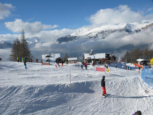 Ein Skigebiet mit Skifahrern und Snowboardern vor einer Bergkulisse.