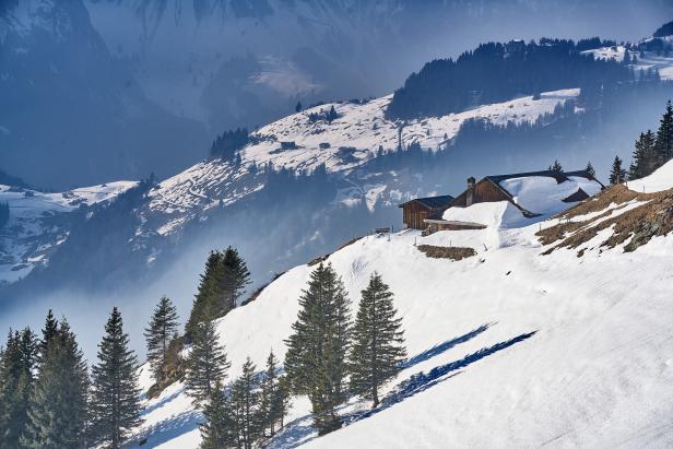 Ein schneebedecktes Holzhaus auf einem Hügel mit Tannenbäumen im Winter.