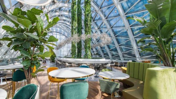 Ein modernes Restaurant mit vielen Pflanzen und einem Glasdach.