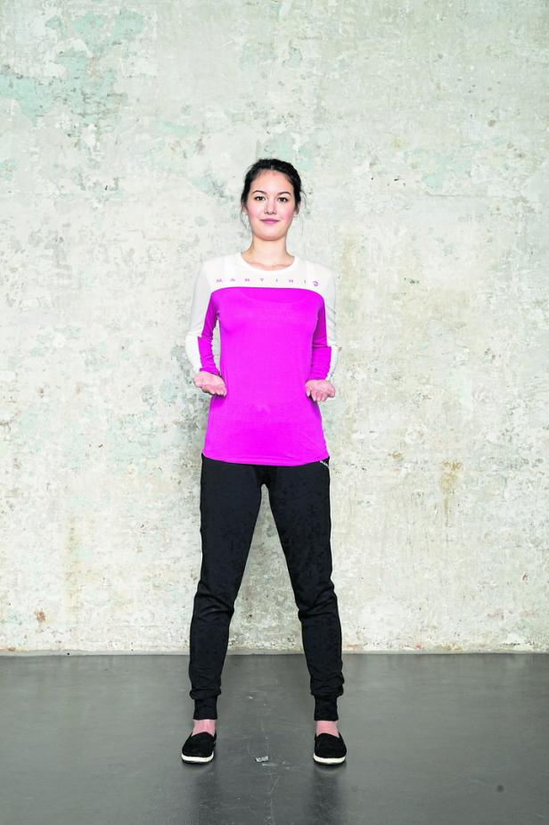 Eine Frau in Sportkleidung steht vor einer grauen Wand.