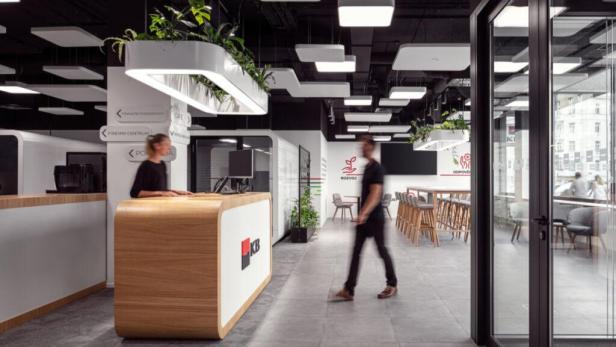 Eine Frau steht an einem Empfangstresen in einer modernen KB Bankfiliale.