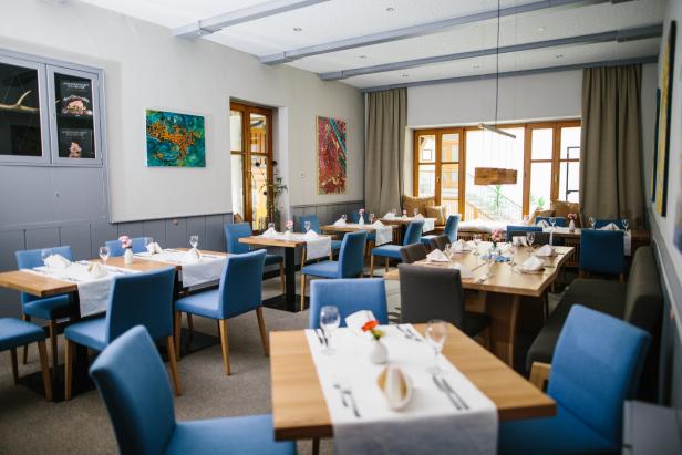 Ein helles Restaurant mit gedeckten Tischen und blauen Stühlen.