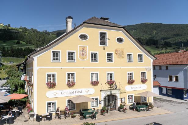 Das Gasthof Post, ein gelbes Gebäude mit blumengeschmückten Fenstern, an einem sonnigen Tag.