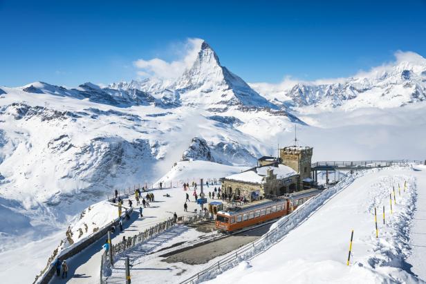Das Matterhorn und eine orangefarbene Zahnradbahn in einer verschneiten Berglandschaft.