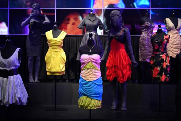 Mehrere Kleider auf Schaufensterpuppen und Mannequins auf einer dunklen Bühne.