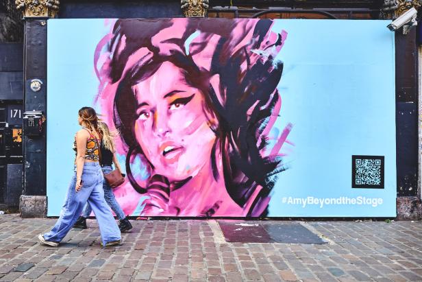Ein farbenfrohes Wandgemälde von Amy Winehouse mit zwei Passanten im Vordergrund.