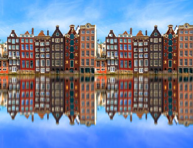 Eine Reihe von bunten Häusern in Amsterdam spiegeln sich im Wasser.
