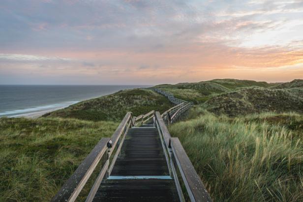 Ein Holzsteg führt durch die Dünenlandschaft zum Meer.
