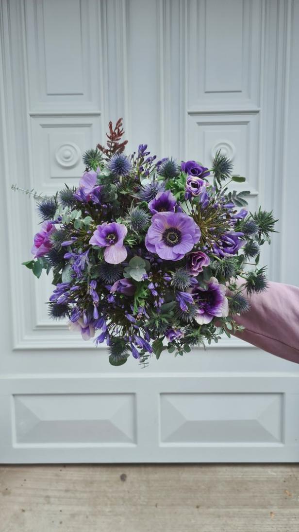 Ein üppiger, violetter Blumenstrauß wird vor einer weißen Tür gehalten.