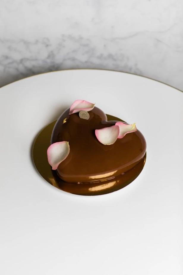 Ein herzförmiger, schokoladenglasierter Kuchen ist mit Rosenblättern dekoriert.