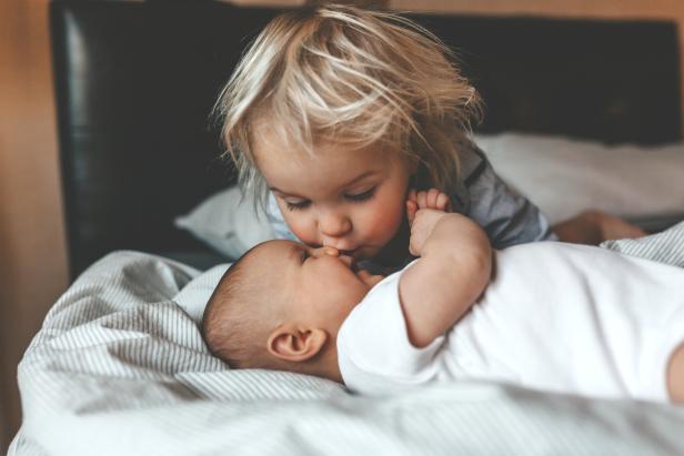 Ein Kleinkind gibt einem Baby einen Kuss auf die Wange.