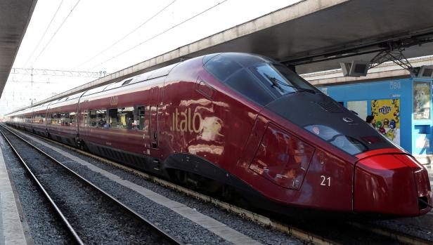 Ein roter Hochgeschwindigkeitszug der Marke Italo steht auf einem Bahnhof.