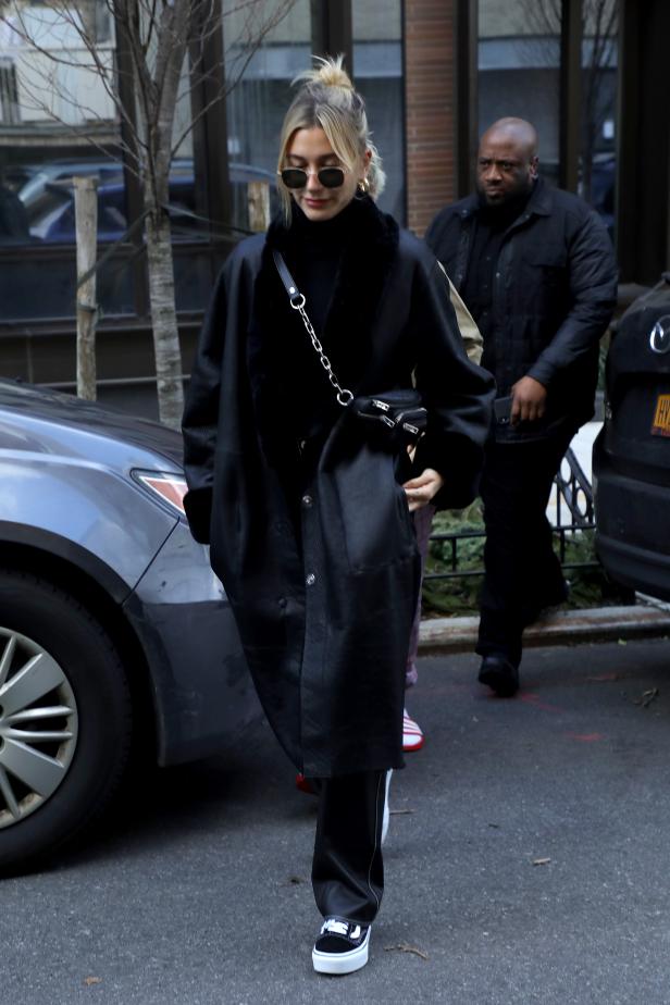 Hailey Bieber trägt einen schwarzen Mantel und eine kleine Handtasche.