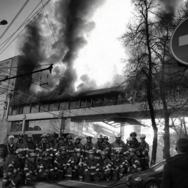 Eine Gruppe Feuerwehrleute posiert vor einem brennenden Gebäude.
