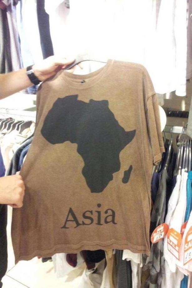 Ein braunes T-Shirt mit einer schwarzen Afrika-Silhouette und dem Wort „Asia“ darauf hängt an einem Kleiderbügel.