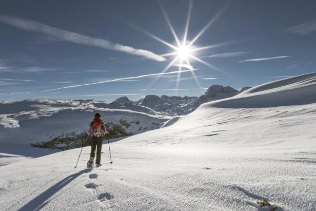 Eine Frau wandert mit Schneeschuhen durch eine verschneite Berglandschaft.