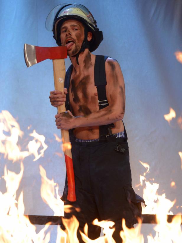 Ein Mann mit Helm und Axt posiert vor einem Feuer.