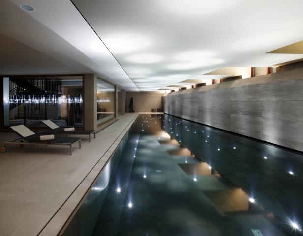 Ein Innenpool mit Liegestühlen und reflektierenden Lichtern an der Wand und im Wasser.