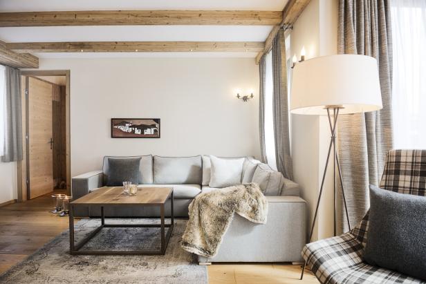 Ein Wohnzimmer mit hellgrauem Sofa, Holzbalkendecke und einem Sessel mit Karomuster.