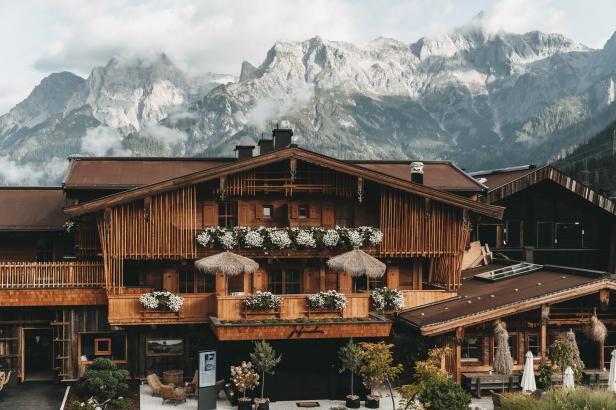 Ein traditionelles Holzhaus mit Blumenkästen vor einer Bergkulisse.