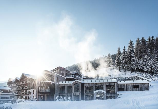 Ein modernes Holzhotel liegt in einer verschneiten Winterlandschaft mit Tannenbäumen.