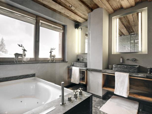 Ein Badezimmer im Chalet-Stil mit Badewanne, Waschtischen aus Stein und Dekorationen mit Hirschen.