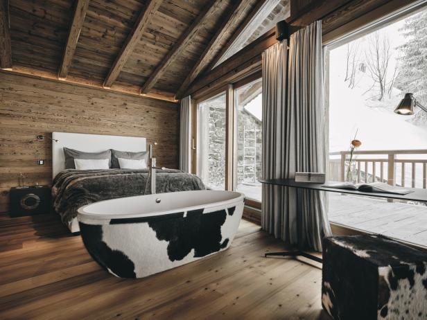 Ein Schlafzimmer im Chalet-Stil mit einer freistehenden Badewanne im Kuhfellmuster.