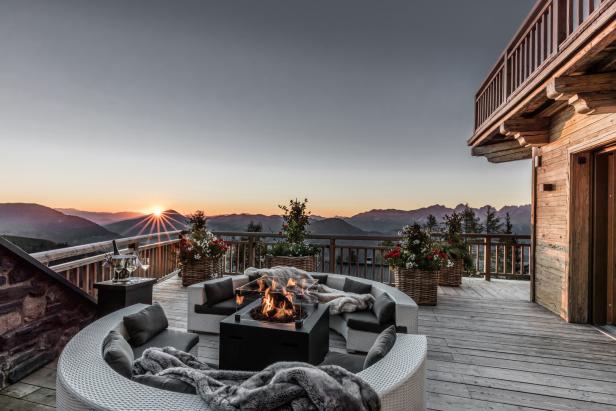 Auf einer Terrasse mit Bergblick stehen Loungemöbel und ein Kamin.