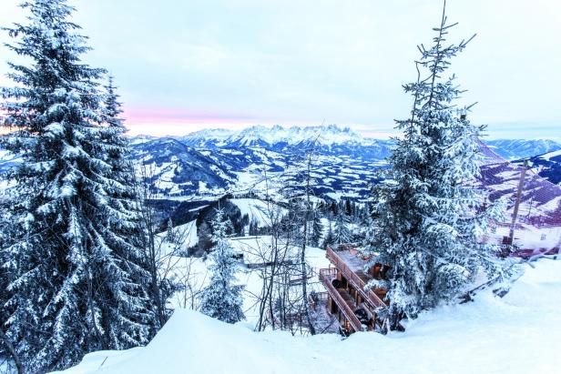 Winterlandschaft mit schneebedeckten Bergen und einem hölzernen Gebäude im Vordergrund.