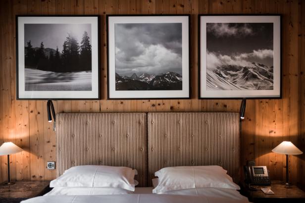 Ein Hotelzimmer mit einem Bett und drei gerahmten Schwarzweißbildern von Berglandschaften an der Holzwand.