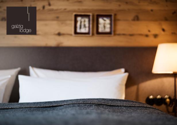 Ein Bett mit grauer Decke und weißen Kissen in der Galzig Lodge.