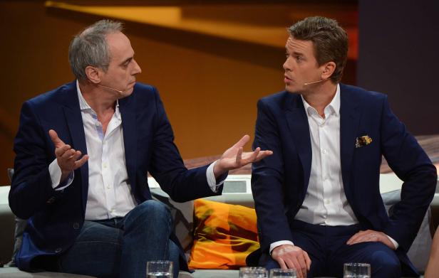 Zwei Männer in Anzügen sitzen auf einer Couch und diskutieren.