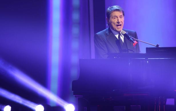 Paul Anka singt am Klavier auf einer Bühne mit blauem Licht.