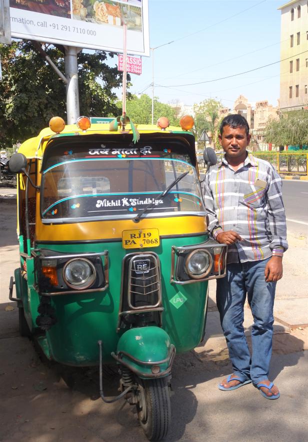 Ein Mann steht neben einem gelb-grünen Bajaj-Tuk-Tuk in Indien.
