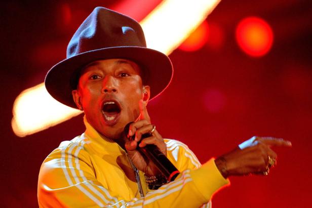 Pharrell Williams tritt in einem gelben Trainingsanzug und Hut auf und singt in ein Mikrofon.