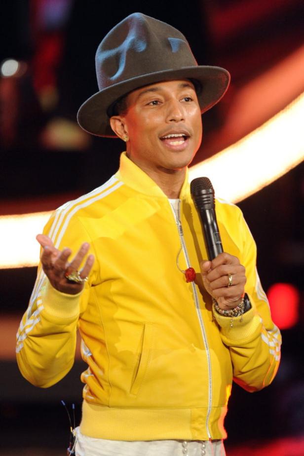 Pharrell Williams tritt in einer gelben Jacke und einem Hut auf einer Bühne auf.