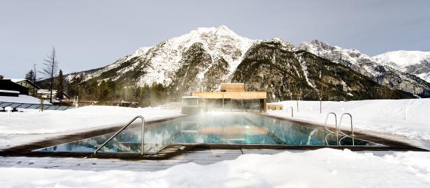 Ein Außenpool mit warmem Wasser vor einer verschneiten Bergkulisse.