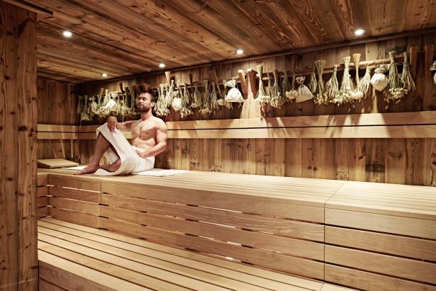 Ein Mann sitzt mit einem Handtuch bekleidet in einer holzvertäfelten Sauna.