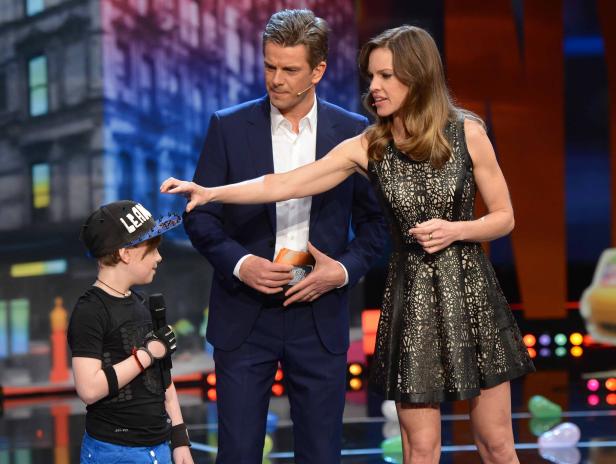 Hilary Swank und Josh Duhamel mit einem Kind auf einer Bühne.