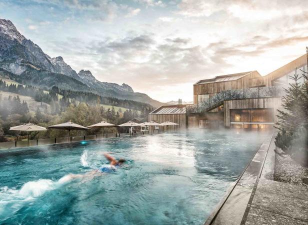 Eine Person schwimmt in einem Außenpool mit Blick auf eine Berglandschaft.