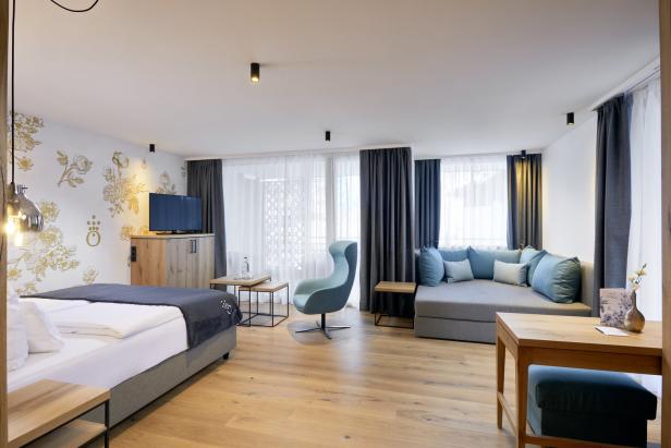 Ein helles Hotelzimmer mit Doppelbett, Sofa und Sessel.