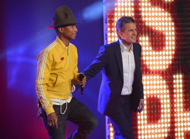 Pharrell Williams und ein Mann im Anzug stehen auf einer Bühne vor einer LED-Wand.