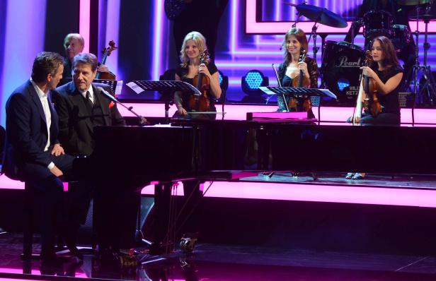 Zwei Männer sitzen am Klavier, begleitet von einem Streichquartett auf der Bühne.