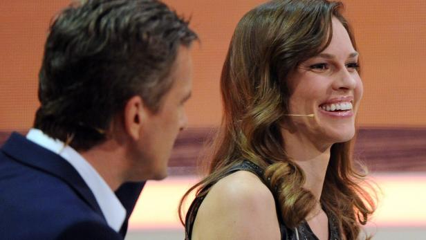 Hilary Swank lächelt auf einer Bühne, während ein Mann sie ansieht.